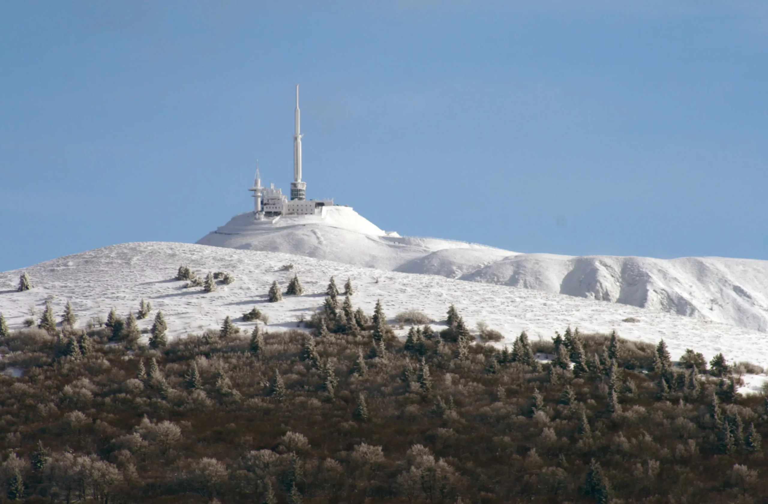 Snow-covered mountain with communication towers under blue sky