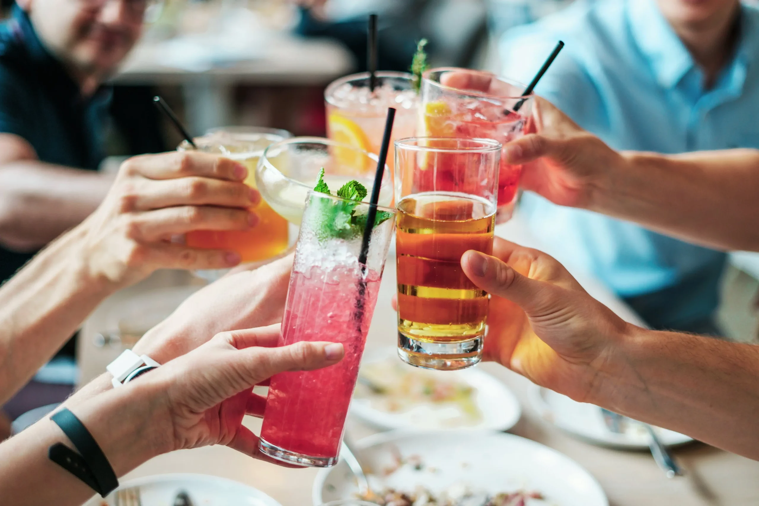 Friends toasting colorful cocktails and beer at table