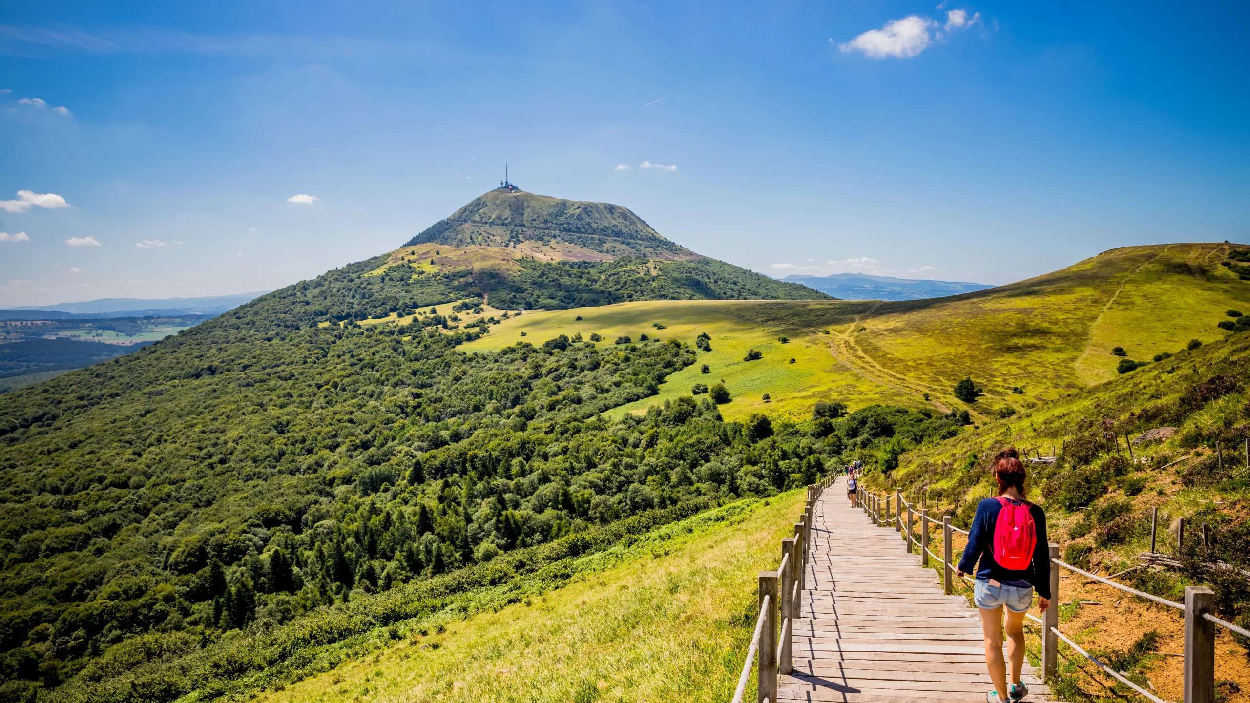 Hiker walking on boardwalk toward green mountain peak