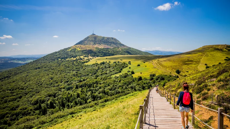 Hiker walking on boardwalk toward green mountain peak
