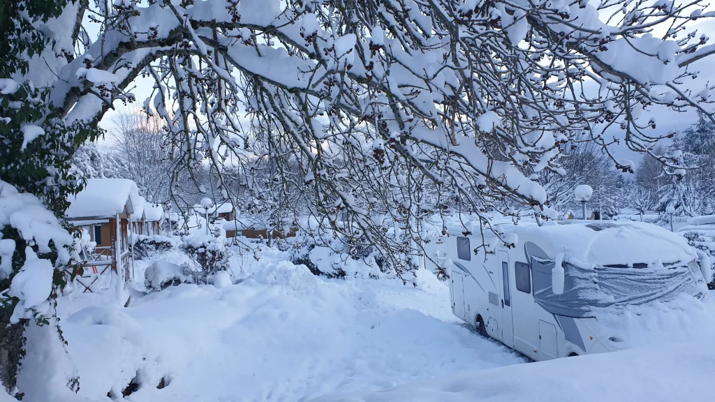 Snow-covered RV and cabins under winter trees