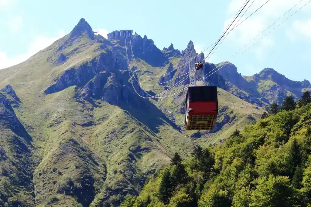 Red cable car ascending green mountain peak