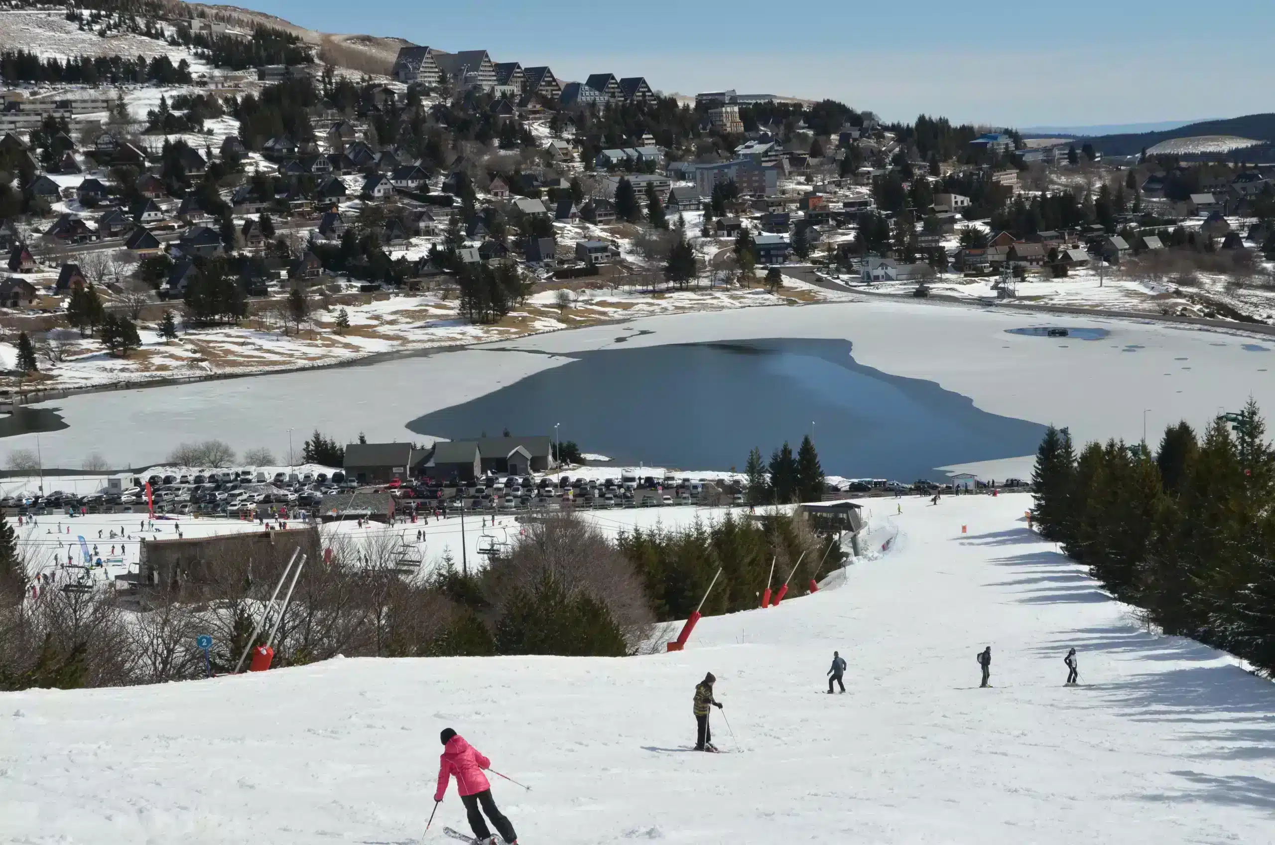 Skiers descending slope above frozen mountain lake